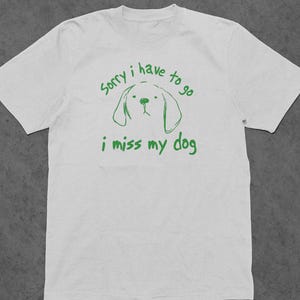 May include: White t-shirt with green text that reads "Sorry I have to go I miss my dog" and a simple line drawing of a dog's head.