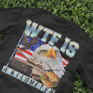 May include: Black t-shirt with a graphic print of an eagle, a tank, and an American flag. The text "WTF IS A KILOMETER" is printed on the shirt.