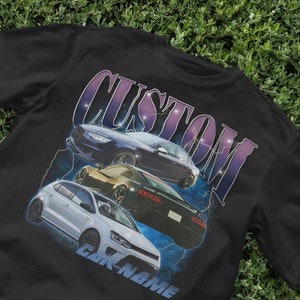 May include: Black t-shirt with a graphic print of three cars and the word "CUSTOM" in a stylized font. The cars are a white Volkswagen, a black Porsche, and a blue Audi. The text "CAR NAME" is printed below the cars.