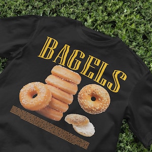 May include: Black t-shirt with the word "BAGELS" printed in yellow on the front. The shirt features a graphic of a stack of bagels with sesame seeds.