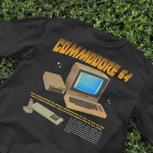 May include: Black t-shirt with a graphic of a Commodore 64 computer, a joystick, and a disk drive. The text "COMMODORE 64" is in yellow and the text below reads "THE COMMODORE 64, OFTEN ABBREVIATED AS C64, IS ONE OF THE MOST ICONIC AND BEST-SELLING HOME COMPUTERS OF ALL TIME."