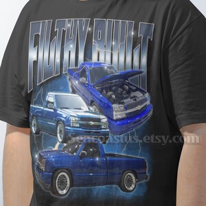 Può includere: T-shirt nero con grafica di tre pick-up blu e la scritta "FILTHY BUILT". Il design include un camion con il cofano aperto. L'URL del negozio Etsy è visibile.