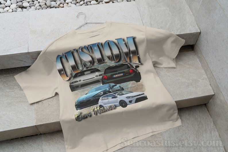 以下が含まれることがあります： ベージュのTシャツに、4台の車が描かれたグラフィックプリントと、スタイリッシュなフォントで「CUSTOM」という文字がプリントされています。「Car Mania」という文字が車の下にプリントされています。