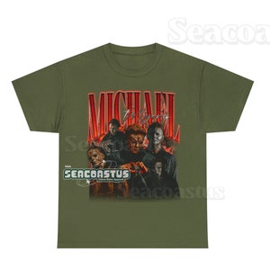 May include: Green t-shirt with a red graphic of Michael Myers from the Halloween franchise. The graphic features multiple images of Michael Myers from different movies in the franchise. The text "MICHAEL Myers" is written in red above the graphic. The text "SEACOASTUS Urban Retro Apparel" is written in white below the graphic.