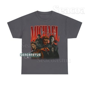 May include: A dark gray t-shirt with a vintage-style graphic of Michael Myers from the Halloween franchise. The graphic features multiple images of Michael Myers in different masks and poses. The text "MICHAEL MYERS" is written in a bold, red font.