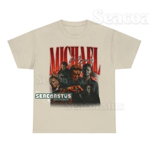 May include: A beige t-shirt with a graphic print of Michael Myers from the Halloween franchise. The graphic features multiple images of Michael Myers in different poses, with the text "MICHAEL MYERS" in red letters above the images. The text "SEACOASTUS Urban Retro Apparel" is printed in green letters below the graphic.