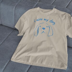 May include: A beige t-shirt with a blue graphic of a dog and the text "i miss my dog".