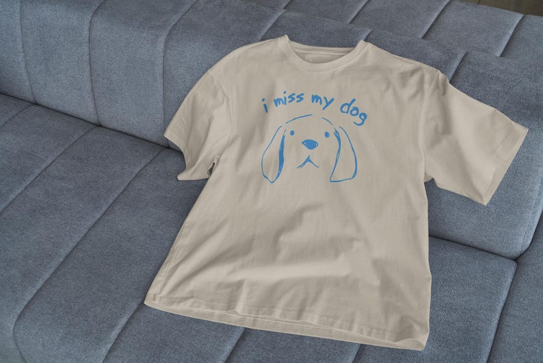 May include: A beige t-shirt with a blue graphic of a dog and the text "i miss my dog".