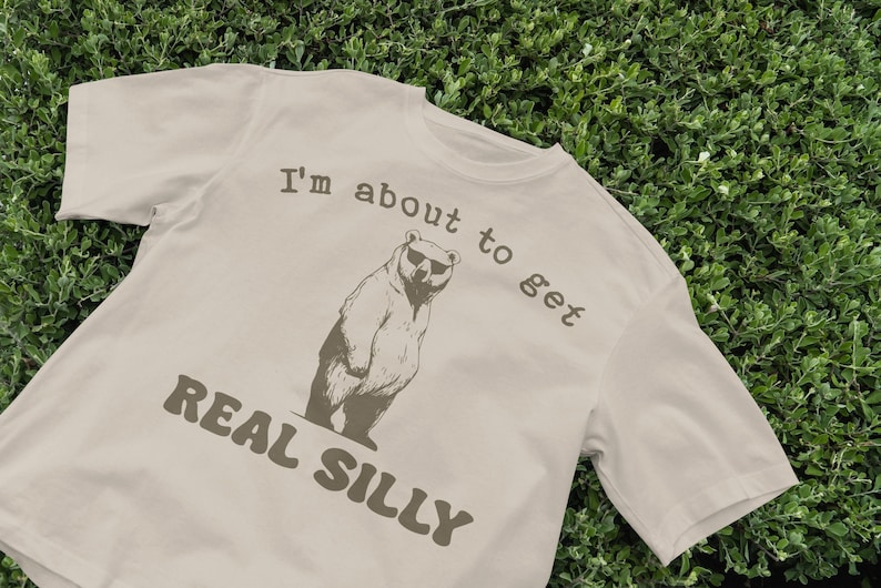 May include: A beige t-shirt with a brown bear wearing sunglasses and the text "I'm about to get REAL SILLY".