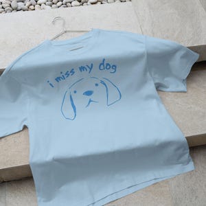 May include: A light blue t-shirt with the text "i miss my dog" and a simple line drawing of a dog's head.