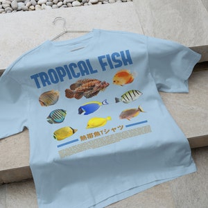 May include: A light blue t-shirt with the text "TROPICAL FISH" printed in blue. The shirt features a variety of colorful tropical fish illustrations.