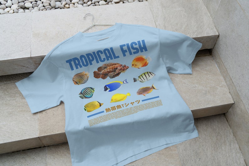 May include: A light blue t-shirt with the text "TROPICAL FISH" printed in blue. The shirt features a variety of colorful tropical fish illustrations.