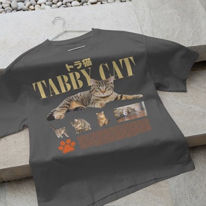 May include: A dark gray t-shirt with the text "Tabby Cat" in gold lettering and a picture of a tabby cat. The text "トラ猫" is also on the shirt.