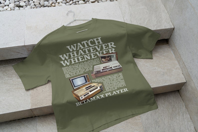 May include: A green t-shirt featuring a vintage advertisement for a Betamax player. The text reads "Watch Whatever Whenever Betamax Player".