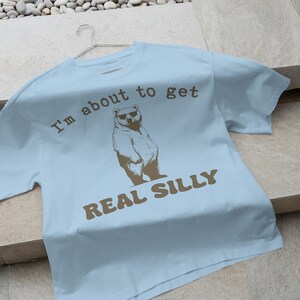 May include: Light blue t-shirt with a brown bear wearing sunglasses and the text "I'm about to get real silly".
