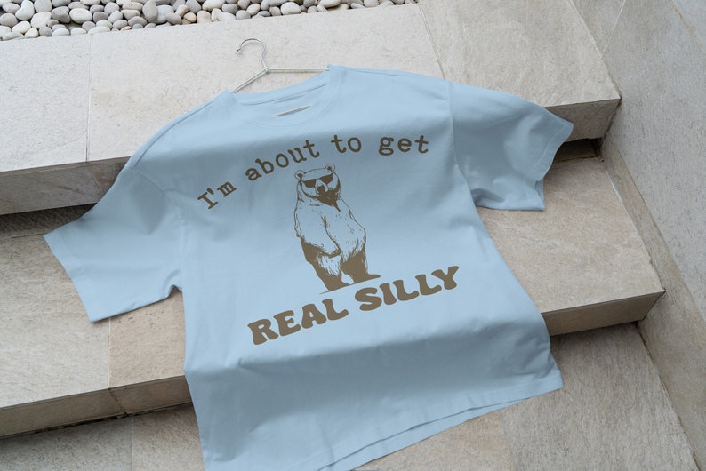 May include: Light blue t-shirt with a brown bear wearing sunglasses and the text "I'm about to get real silly".