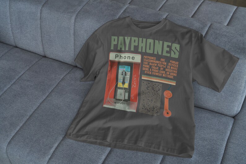 May include: Dark gray t-shirt featuring a graphic of a payphone booth with the word "PAYPHONES" in green. The shirt includes text describing payphones as public telecommunication devices.
