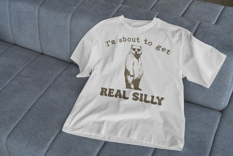 May include: White t-shirt with a brown bear wearing sunglasses and the text "I'm about to get real silly".