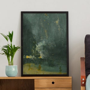 Puede incluir: Una pintura abstracta enmarcada con fondo verde oscuro y detalles dorados cuelga sobre un armario de madera con dos cajones. Una manta de lana azul claro está colocada sobre un sillón gris oscuro.