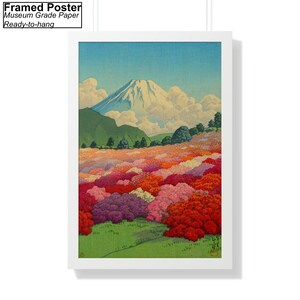 Op de afbeelding: Een ingelijste poster met een Japanse landschapschildering van de berg Fuji met een veld met roze, rode en witte bloemen op de voorgrond. De lucht is blauw met witte wolken.
