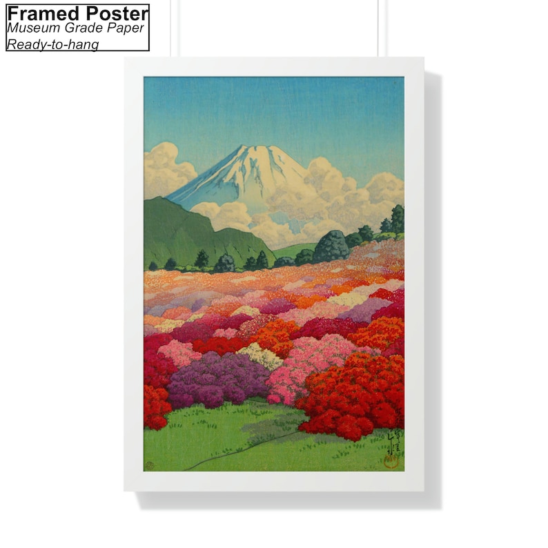 Op de afbeelding: Een ingelijste poster met een Japanse landschapschildering van de berg Fuji met een veld met roze, rode en witte bloemen op de voorgrond. De lucht is blauw met witte wolken.