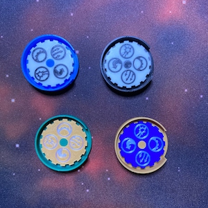 Może przedstawiać: Cztery różne kolorowe, obracające się koła z tworzywa sztucznego z różnymi symbolami. Koła są niebieskie, czarne, zielone i złote.