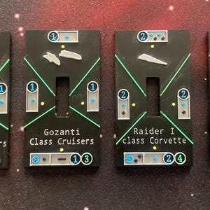 May include: Four black game tokens with white text and green and white accents. The tokens are labeled "Gozanti Assault Cruisers", "Gozanti Class Cruisers", "Raider I class Corvette", and "Raider II class Corvette".