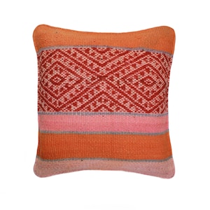 Könnte beinhalten: Quadratisches Zierkissen mit gewebtem Design. Das Kissen hat ein zentrales geometrisches Muster in Rot und Hellrosa, das von horizontalen Streifen in Orange, Rosa und Grau umrandet ist. Die Kanten des Kissens sind dunkler Orange.