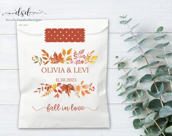 May include: A white favour bag with a fall-themed design featuring orange, red, and yellow leaves. The bag has the text "Olivia & Levi" and "fall in love" printed on it. The date "11.30.2023" is also printed on the bag.