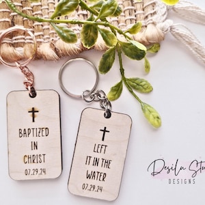 May include: Two wooden keyrings with a cross design and engraved text. The first keyring says "Baptized in Christ 07.29.24". The second keyring says "Left it in the water 07.29.24".
