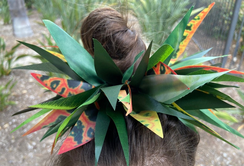 May include: A green and orange floral hair clip with a leafy design. The clip is made of fabric and has a vibrant colour scheme.