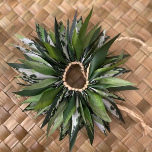 May include: A green and white lei made of leaves, tied together with a brown string.