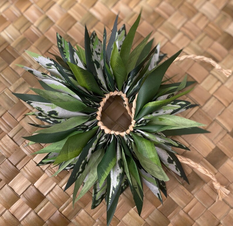 May include: A green and white lei made of leaves, tied together with a brown string.