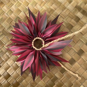 May include: A red and black lei made of fabric leaves, tied together with a brown cord.