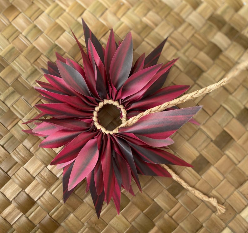 May include: A red and black lei made of fabric leaves, tied together with a brown cord.