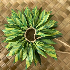 May include: A green and yellow lei made of fabric leaves, tied together with a brown string.