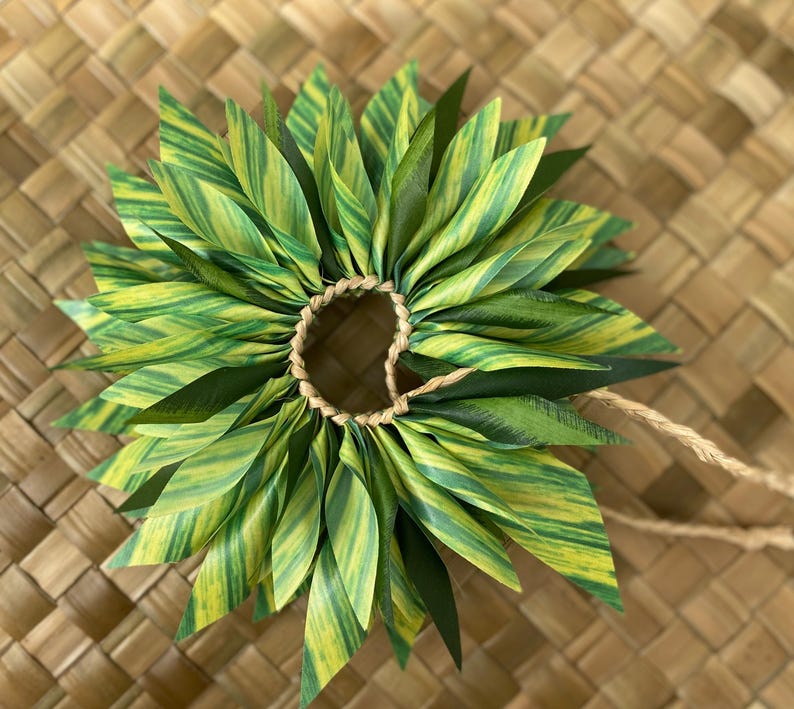 May include: A green and yellow lei made of fabric leaves, tied together with a brown string.