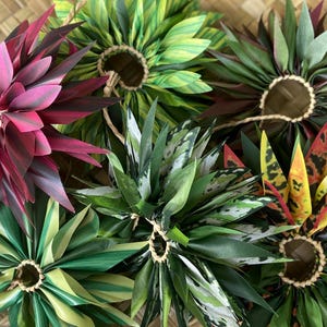 May include: Assortment of colourful handmade flower leis, each with a different pattern and colour. The leis are made of fabric and are tied together with twine.
