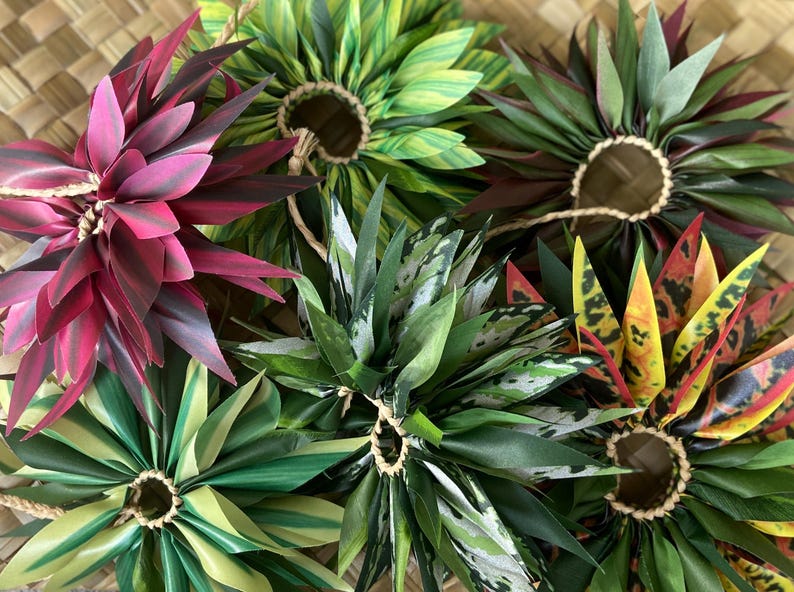 May include: Assortment of colourful handmade flower leis, each with a different pattern and colour. The leis are made of fabric and are tied together with twine.