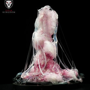 Puede incluir: Una escultura de resina rosa y blanca de una criatura con una estructura en forma de telaraña. La escultura está sobre una base negra.