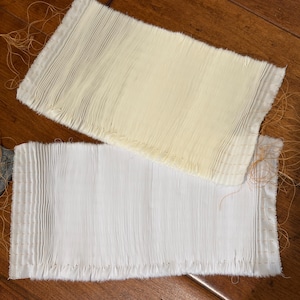 May include: Two rectangular pieces of fabric featuring vertical smocking with light orange thread. One piece is off-white and the other is bright white. Both pieces have raw, unfinished edges with loose orange thread ends extending from the sides.