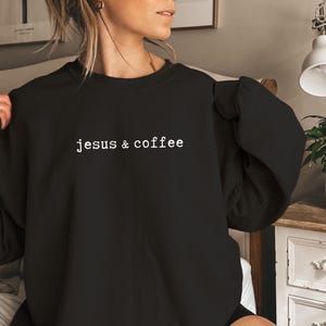 May include: Black crew neck sweatshirt with the text "jesus & coffee" in a white, sans-serif font. The sweatshirt is a solid black color and has long sleeves. The text is centered on the chest.