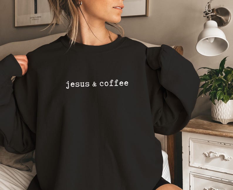 May include: Black crew neck sweatshirt with the text "jesus & coffee" in a white, sans-serif font. The sweatshirt is a solid black color and has long sleeves. The text is centered on the chest.