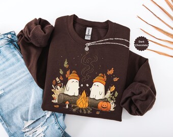 May include: Dark chocolate-colored sweatshirt featuring a whimsical illustration of two ghosts roasting marshmallows over a campfire. The design includes a pumpkin, autumn leaves, and the text "Dark Chocolate". A silver necklace is draped across the sweatshirt.
