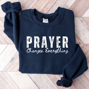 May include: A navy blue sweatshirt with the text "PRAYER Changes Everything" in white distressed lettering.