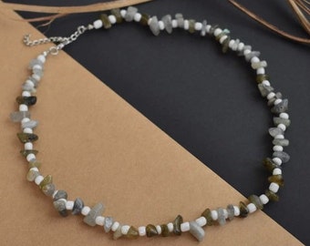 May include: A silver chain necklace with white and grey stone beads. The necklace is on a brown surface.