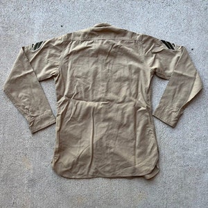 May include: A tan long-sleeved shirt with black and green stripes on the shoulders.