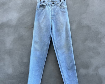 May include: Light blue denim jeans with a high waist and button fly. The jeans have a straight leg and are hanging on a hanger.