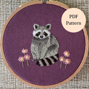 May include: Embroidered hoop art featuring a raccoon with a gray and black striped tail, sitting on a purple background with pink flowers.