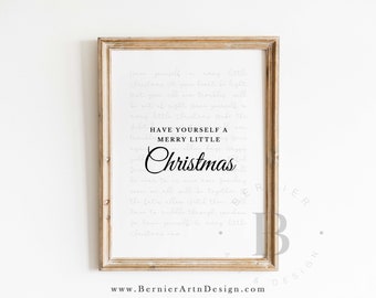 May include: A framed print with a light wood-colored frame. The print features the words "Have yourself a Merry Little Christmas" in a black script font, with the lyrics of the song in a faded gray font in the background. The background is white.